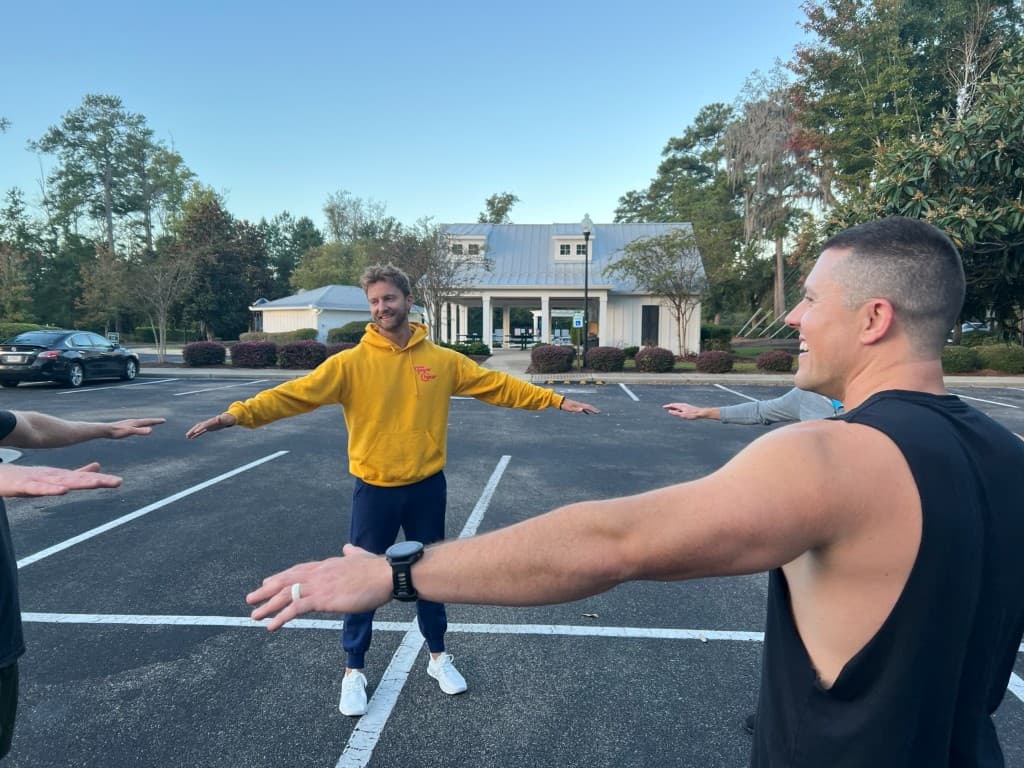 Men in a circle stretching and laughing before the workout in the parking lot